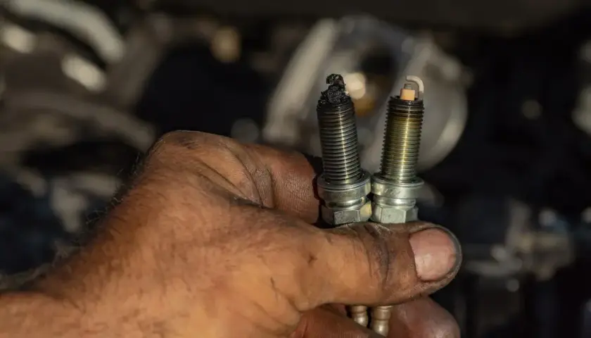 Brudna ręka mechanika pokazuje dwie świece zapłonowe, jedna z osadem, wskazująca na awarię świec żarowych.