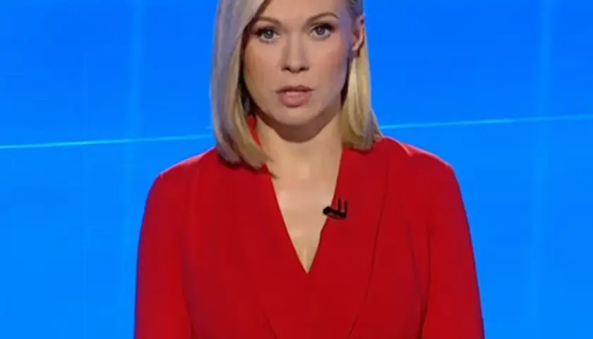 Monika Sawka w czerwonej sukience, z mikrofonem przy dekolcie, na tle niebieskiego ekranu.