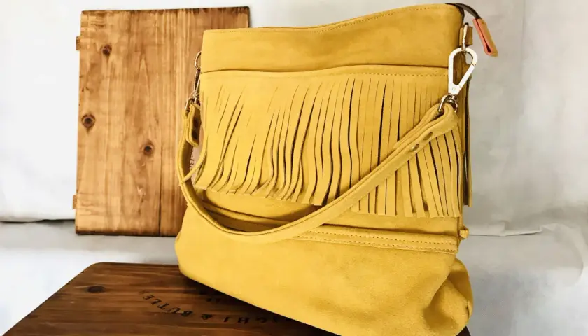 Bolso amarillo con flecos, de ante o serraje, sobre una caja de madera.