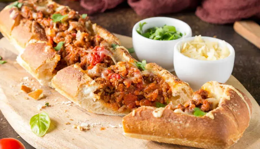 Une baguette farcie généreusement avec une sauce à la viande savoureuse et du fromage fondant, prête à être dégustée.