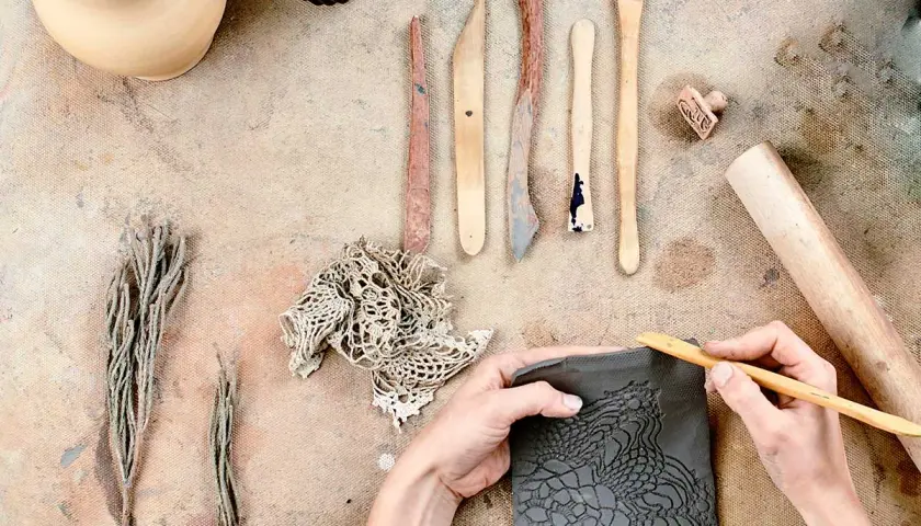 Mani che lavorano con il das adulti, creando un motivo a pizzo su argilla con strumenti da scultore.