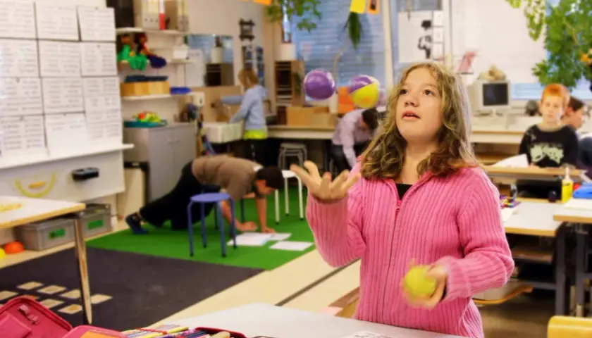 Mädchen jongliert mit Bällen im Klassenzimmer, während andere Kinder lernen. Ein Beispiel für bewegtes Lernen.