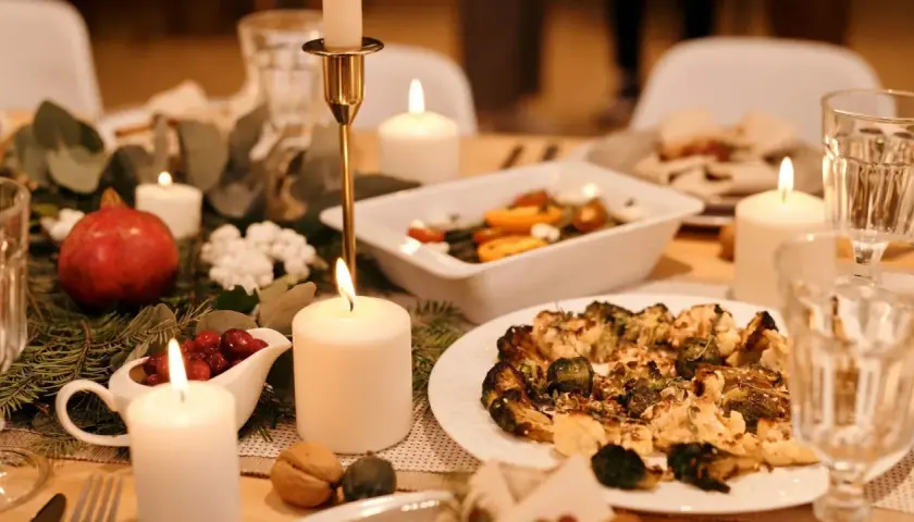 Festlich gedeckter Tisch mit Kerzenlicht, Granatapfel, Cranberry-Sauce und einem Teller mit geröstetem Gemüse – ein gesundes Weihnachtsessen.