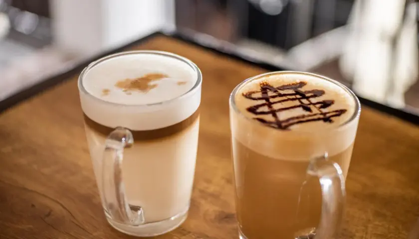 Dwie pyszne kawy latte, jedna z czekoladowym wzorem, druga z pianką i cynamonem. Idealne na chwilę relaksu.