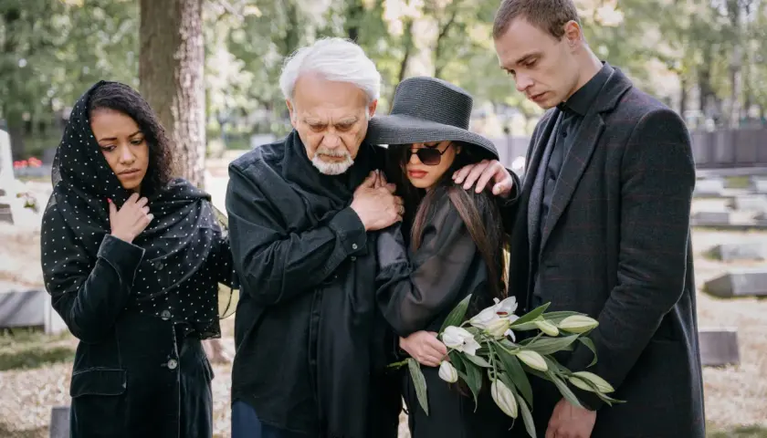 Smutna rodzina na cmentarzu. Eleganckie, ciemne stroje, jak się ubrać na pogrzeb, podkreślają żałobę.