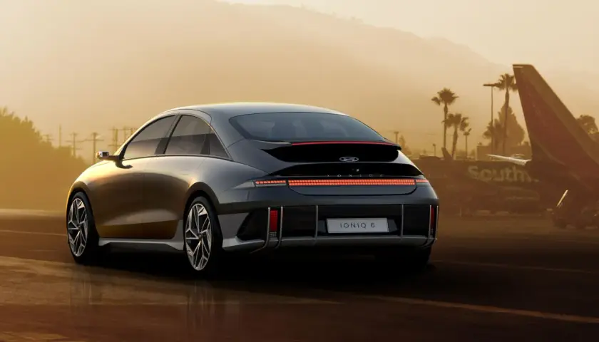 Elegancki Hyundai Ioniq 6 z charakterystycznym pasem świateł z tyłu, zaparkowany na tle lotniska i palm.