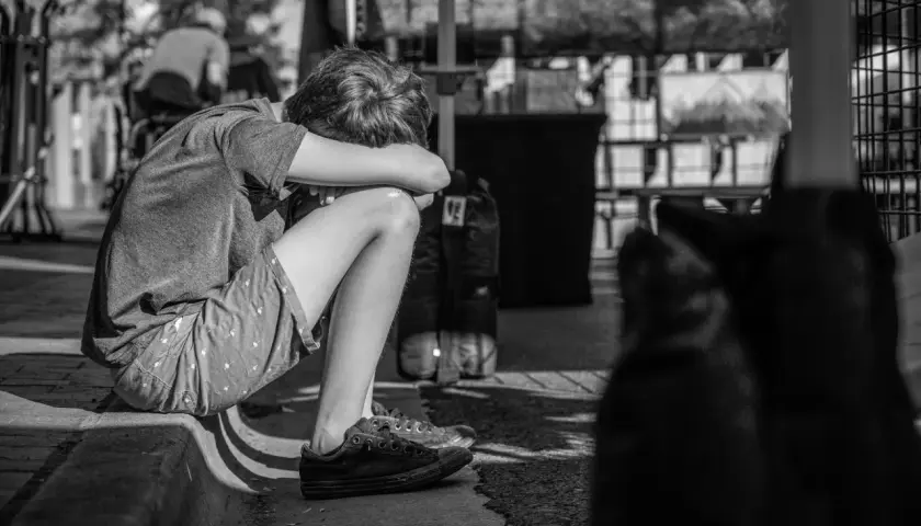 Chłopiec skulony na chodniku, zamyślony. Leczenie psychiatryczne a opieka nad dzieckiem to trudne wyzwania dla rodziny.