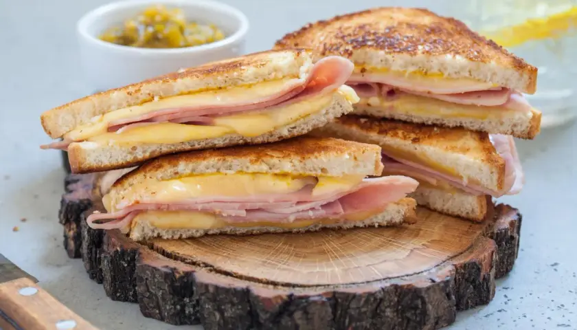 Pile de croque monsieur dorés, garniture généreuse de jambon et fromage fondant, servis sur une tranche de bois rustique.