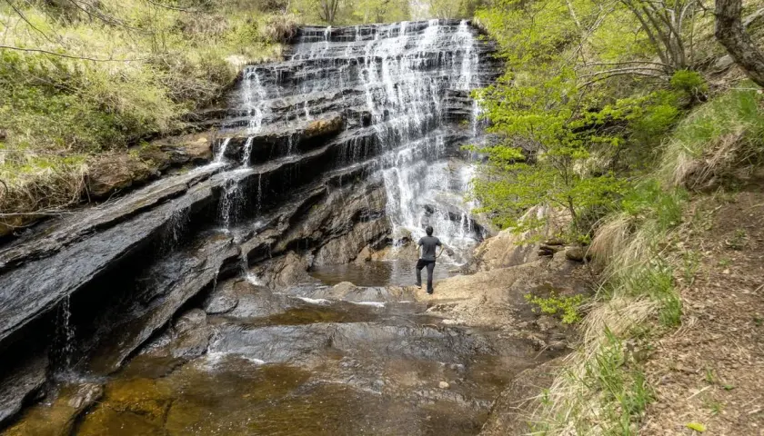 Cascada en un bosque frondoso, ideal para descubrir la **que ver en Burgos naturaleza**. Un hombre contempla la fuerza del agua.