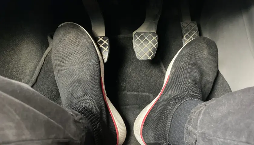 Pies con zapatillas negras listas para arrancar. Hay que pisar el embrague para arrancar el coche.
