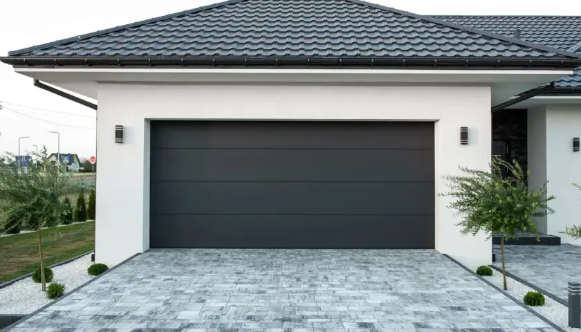 Modernes Haus mit neuem, dunklem Garagendach und gepflasterter Einfahrt.