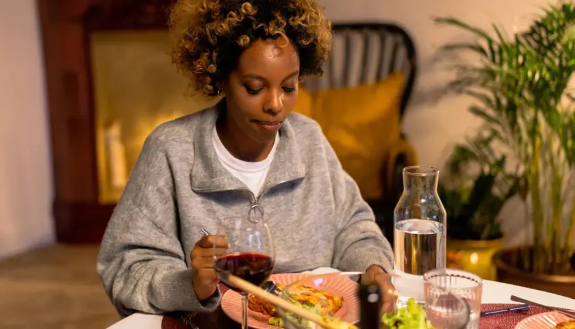 Mujer con cabello rizado mira su plato de comida, pero no come porque no tengo hambre. Hay vino y ensalada en la mesa.