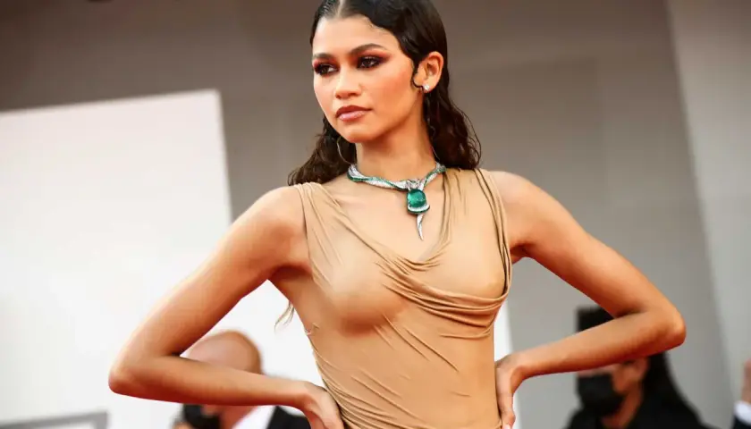 Zendaya med vattenkammat hår, klädd i en beige klänning och en grön ormhalsband.