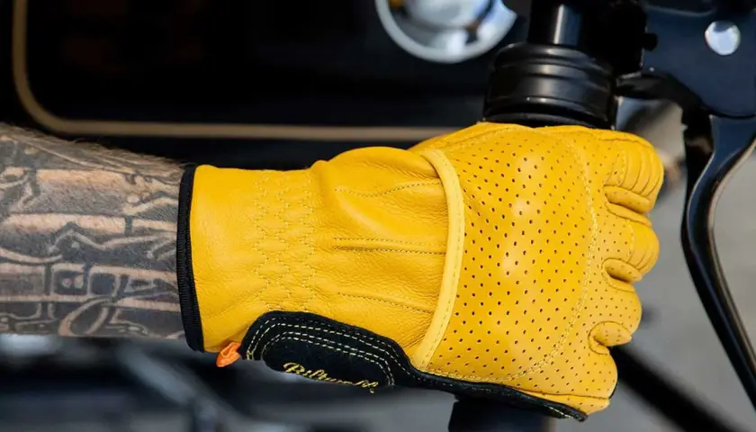 Mano tatuata con guanti Biltwell gialli traforati, pronti per un giro in moto.