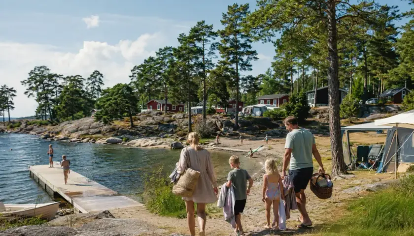 Familj på väg mot vattnet för en härlig semester med bebis i Sverige. Barnen springer glatt mot bryggan där andra badar.