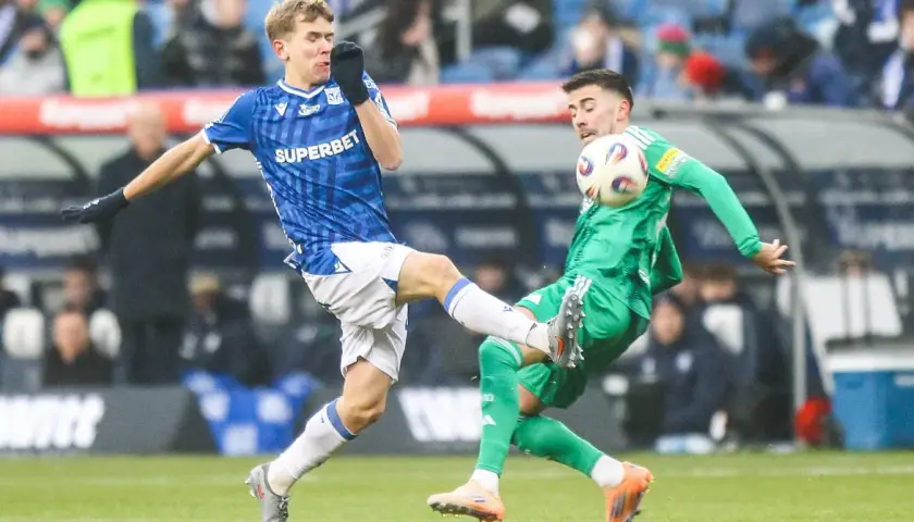 Dwóch piłkarzy walczy o piłkę. Jeden w niebieskiej koszulce, wychowanek Lecha Poznań, próbuje odebrać futbolówkę przeciwnikowi w zielonym stroju.