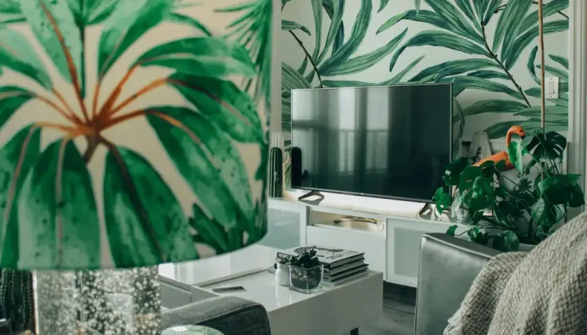 Sala de estar con papel tapiz de hojas tropicales. Muebles DM blancos y un televisor moderno.