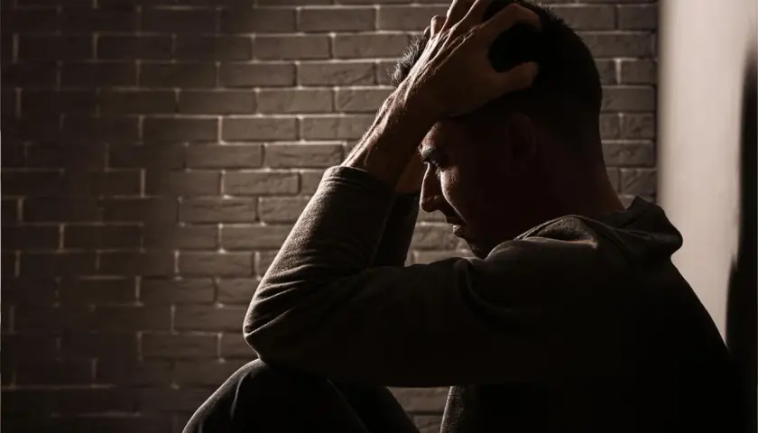 Uomo seduto con le mani tra i capelli, illuminato da un raggio di luce. Potrebbe cercare sollievo con stabilizzatori dell'umore naturali.