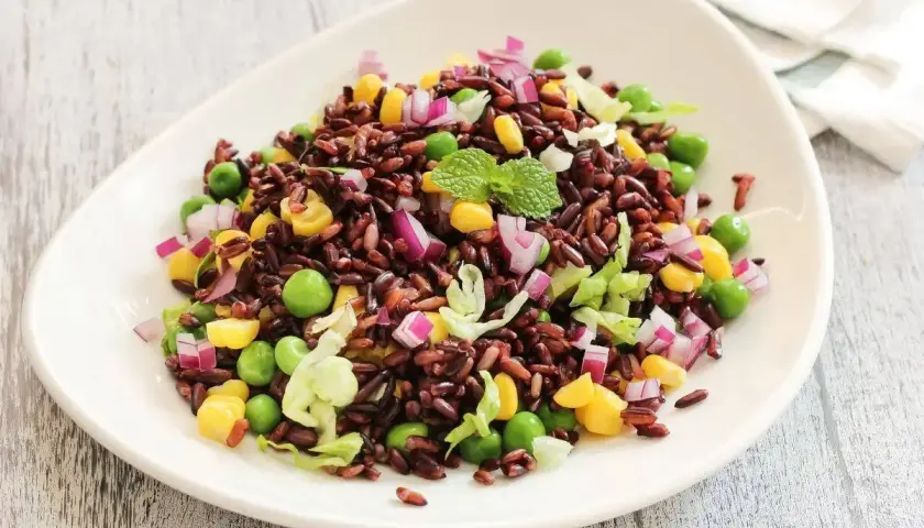 Insalata colorata di riso venere freddo con piselli, mais, cipolla rossa e lattuga. Un'idea fresca su come condire il riso venere freddo.