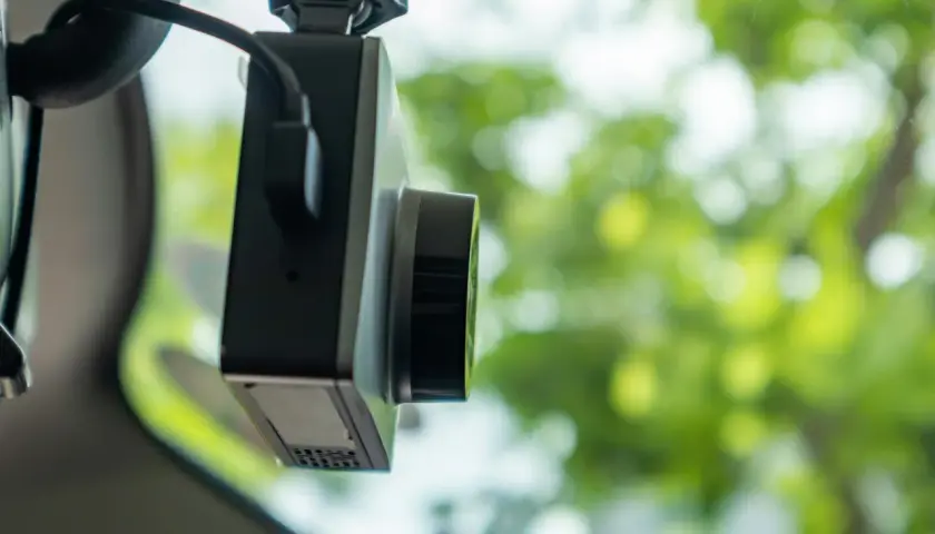 Kamera samochodowa z widocznym obiektywem i kablem. Dowiedz się, jak ustawić g-sensor, aby chronić nagrania w razie wypadku.