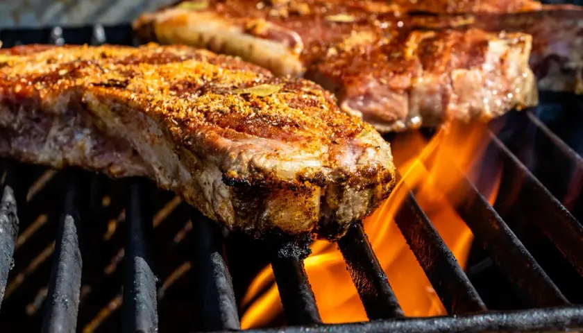 Deux entrecôtes au grill, assaisonnées et grillées à la perfection, avec des flammes vives en dessous.