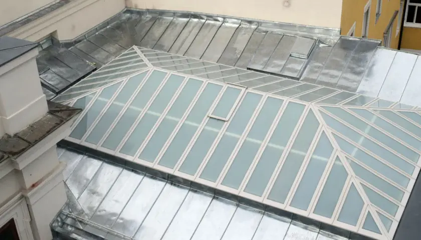 Dachdecker arbeitet an Glasdach-Fugen abdichten. Metallbedecktes Dach mit Glasflächen und einem kleinen Lüftungsfenster.
