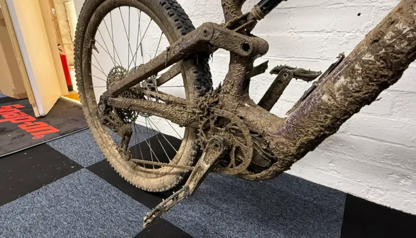 Mud-caked mountain bike rear triangle and wheel. This looks like it will be an expensive bike service cost.