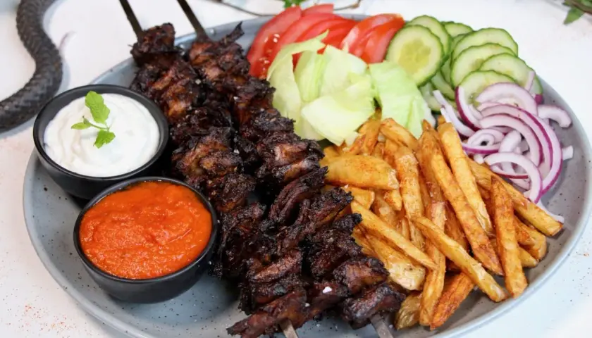 En tallrik med vegetarisk kebab på spett, serverad med pommes frites, sallad, tomat, gurka, rödlök, vit sås och en röd sås.