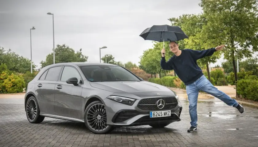 Hombre con paraguas posa junto a un Mercedes Clase A gris. ¡Una prueba de conducción bajo la lluvia!