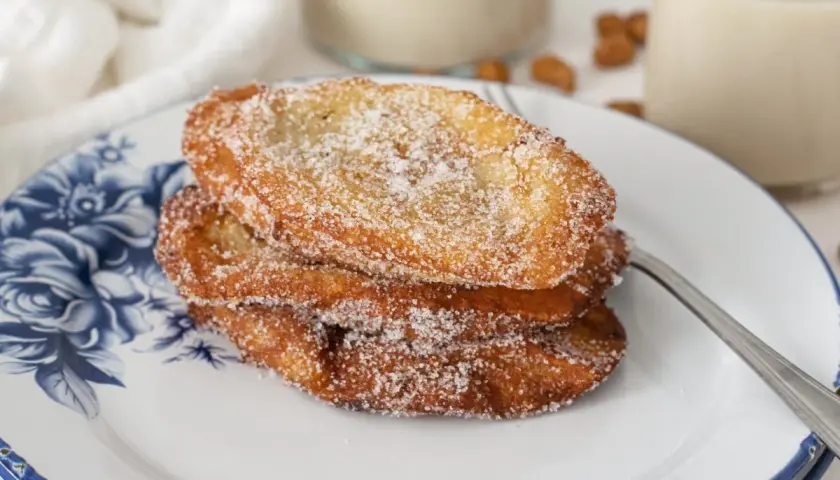 Tres torrijas de horchata, doradas y espolvoreadas con azúcar, apiladas en un plato con diseño floral azul.