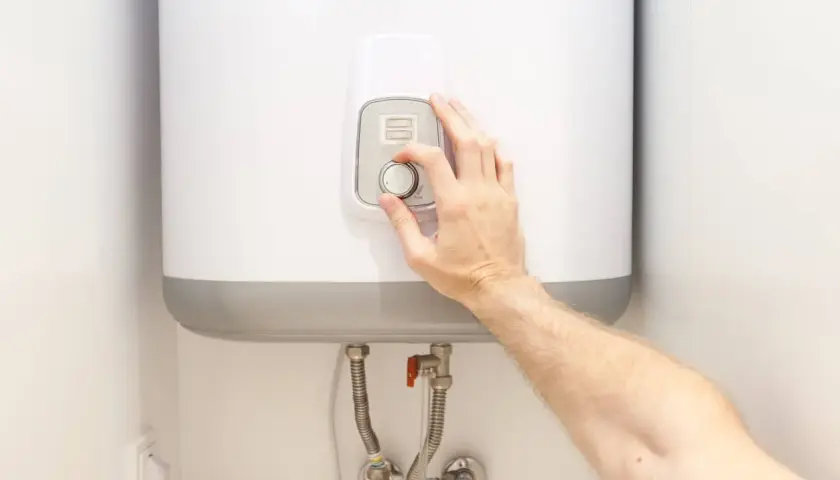 Mano ajustando el control de temperatura de un termo eléctrico.