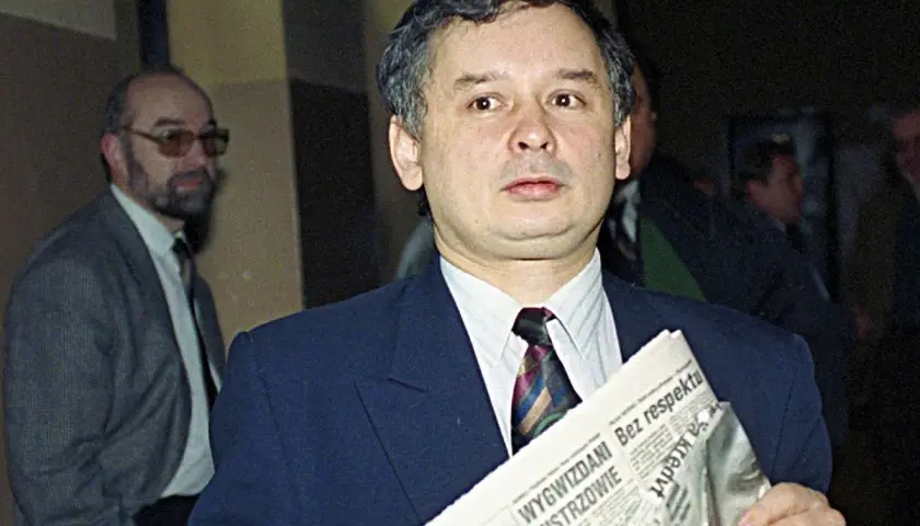 Jarosław Kaczyński z gazetą, zastanawia się, kto ze starej gwardii PiS trafił na "czarną listę". Obok mężczyzna w okularach.