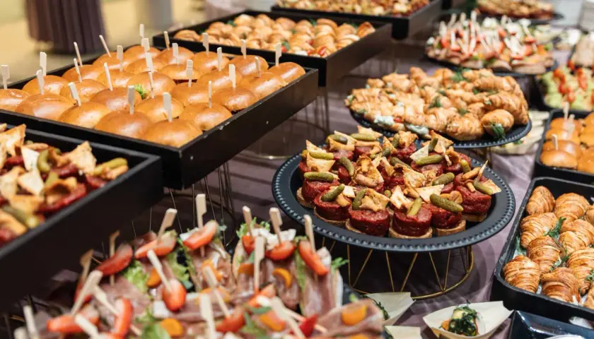 Stół z przekąskami: mini burgery, croissanty, tartinki, koreczki z owocami i mięsem.