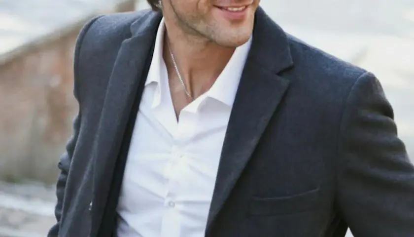 Hombre sonriente con chaqueta gris y camisa blanca, luciendo un estilo look smart casual.