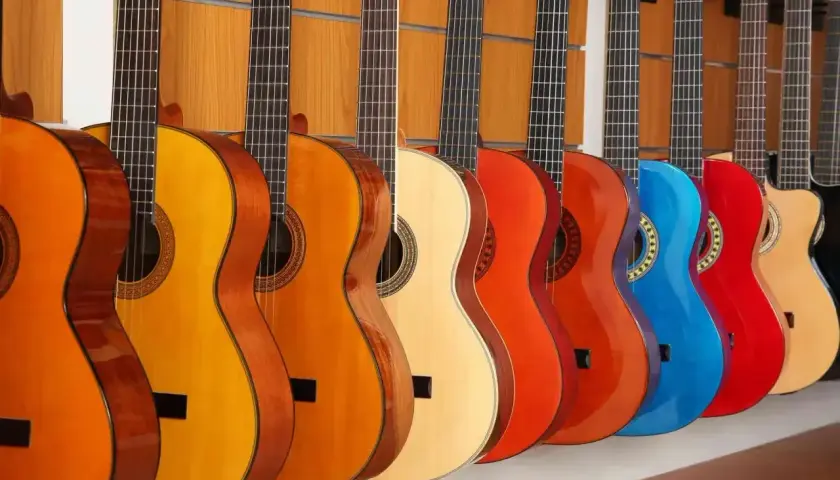Rząd kolorowych gitar akustycznych, od pomarańczowej po czerwoną i niebieską, prezentuje różne rozmiary i odcienie.