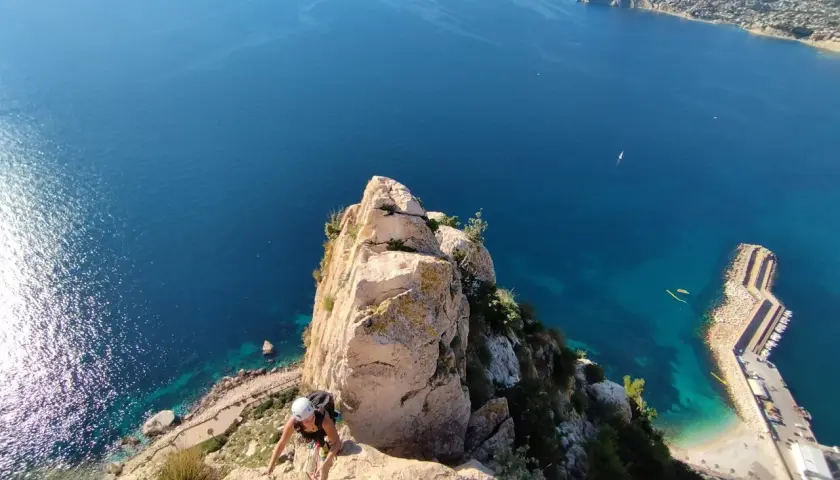 Escaladora en el Peñón de Calpe, con el mar azul y la costa al fondo.