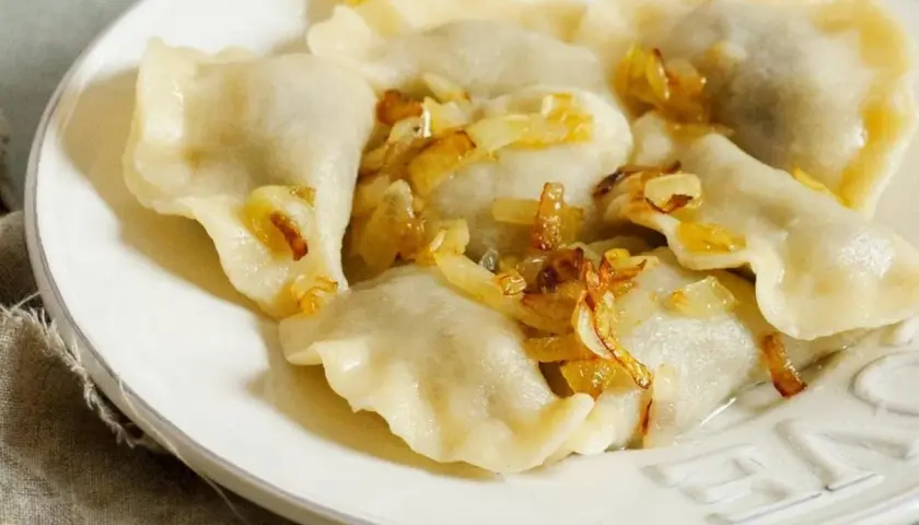 Pyszne pierogi ruskie na talerzu, polane skwarkami z cebulki. Idealne, gdy wiesz, jak długo gotować pierogi ruskie.