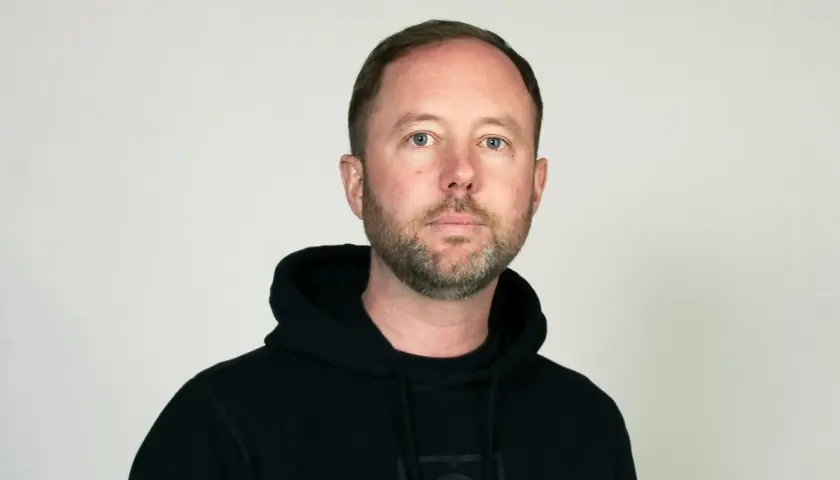 Daniel Holmgren, en man med blå ögon och skägg, bär en svart huvtröja.