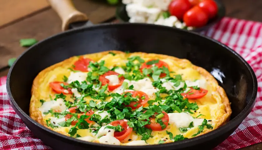 Herzhaftes Omelette mit Feta, Tomaten und Petersilie in einer Pfanne, bereit zum Servieren.