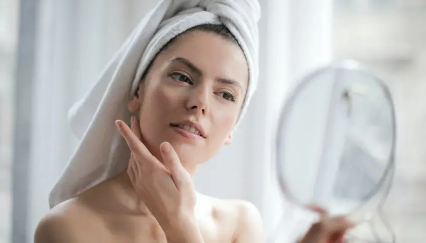 Donna con asciugamano in testa si guarda allo specchio, la sua pelle luminosa grazie all'acido ialuronico e vitamina C insieme.