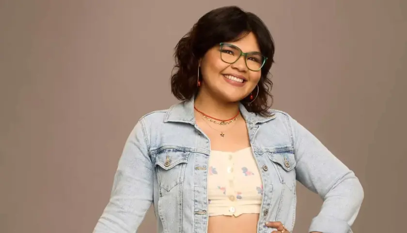 Belissa Escobedo, souriante, porte une veste en jean et des lunettes vertes. Elle est connue pour ses rôles dans des films et séries TV.