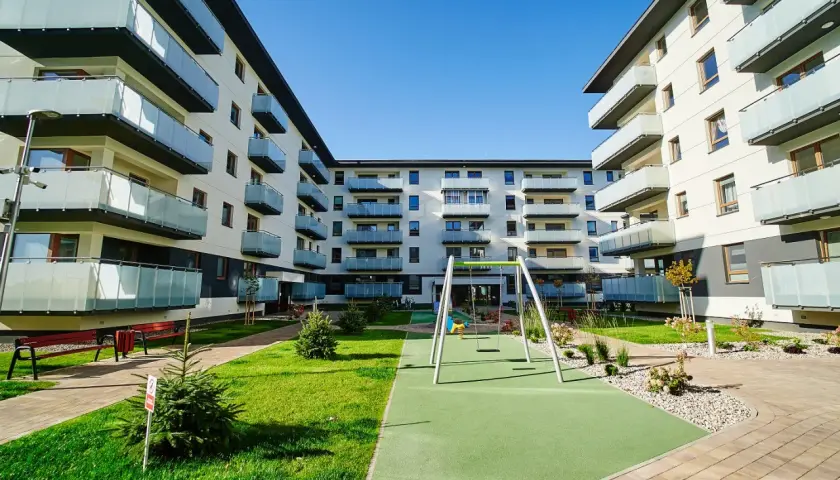 Nowoczesny **piano park** z placem zabaw i zielenią między budynkami mieszkalnymi.