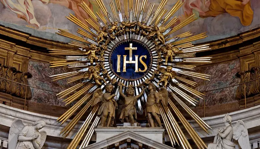 Goldene Strahlenkrone mit IHS-Symbol, das für Jesus steht. Putten und Engel umgeben das Symbol, das die göttliche Bedeutung von IHS unterstreicht.