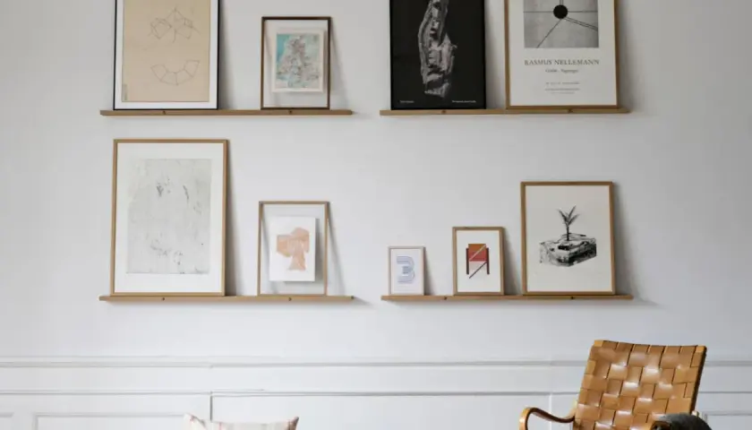 Bilderleiste dekorieren wohnzimmer: Mehrere gerahmte Kunstwerke und Karten zieren zwei schlichte Holzregale, die eine stilvolle Wandgestaltung im Wohnzimmer bilden.