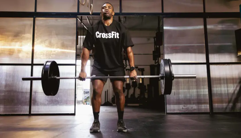 Mężczyzna w koszulce CrossFit podnosi sztangę na siłowni.