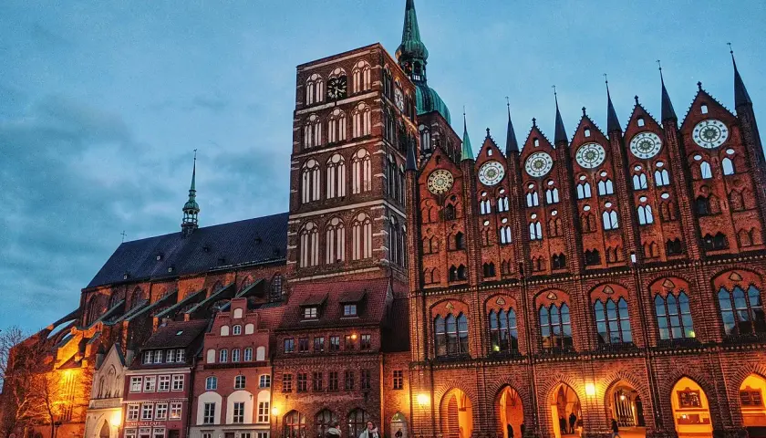 Abendstimmung im **Stralsund Zentrum**: imposante Backsteingotik mit Kirchturm und Rathaus, beleuchteter Marktplatz mit wenigen Passanten.