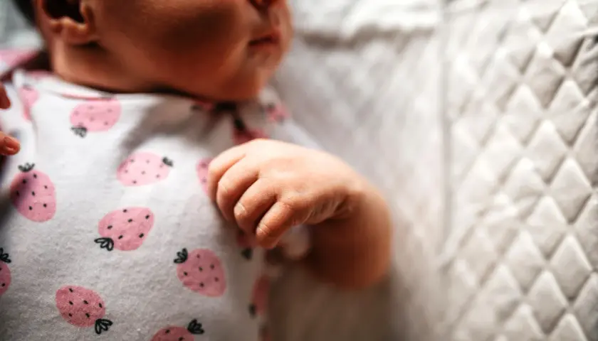 Małe niemowlę zaciska piąstki i się napina, ubrany w pajacyk w truskawki.