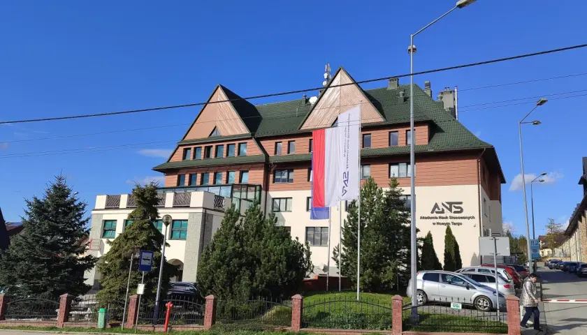 Budynek Akademii Nauk Stosowanych w Nowym Targu z polską flagą.