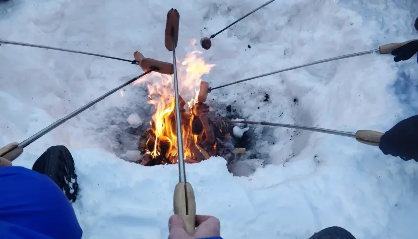 Ludzie pieką kiełbaski nad ogniskiem zimą. Płomienie tańczą, a śnieg otacza ciepło.