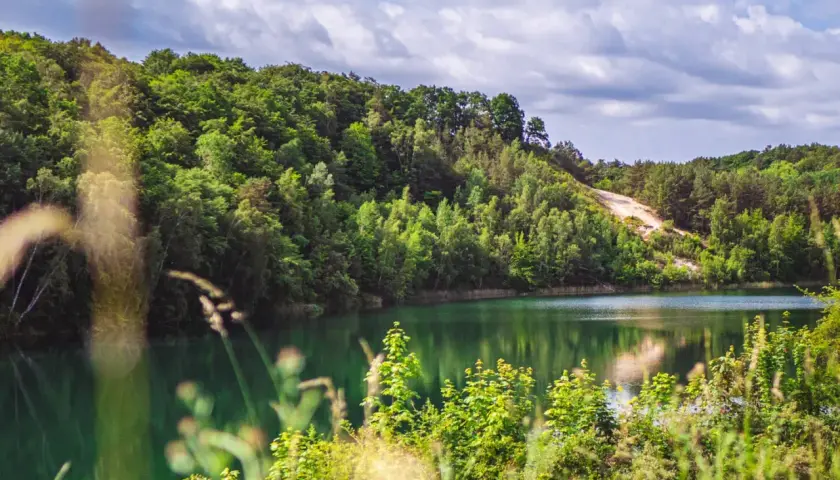Turkusowe jezioro Wapnica otoczone bujną zielenią, z piaszczystym zboczem w tle.